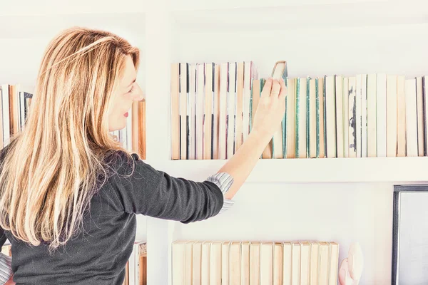 Hermosa joven tomando un libro de estantería en la biblioteca —  Fotos de Stock