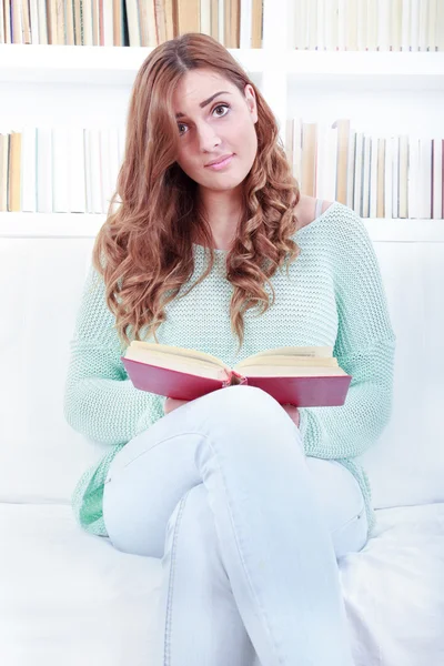 Porträtt av förvirrad härlig kvinna läser en bok i hennes levande r — Stockfoto