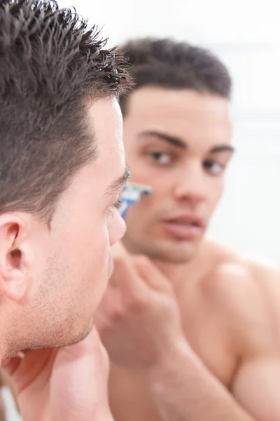 Man with reflection in mirror shaving his face — Stock Photo, Image