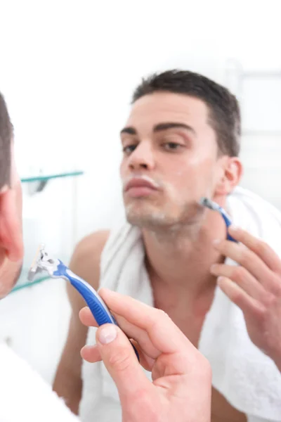 Отражение молодого человека, бреющегося в зеркале ванной комнаты — стоковое фото