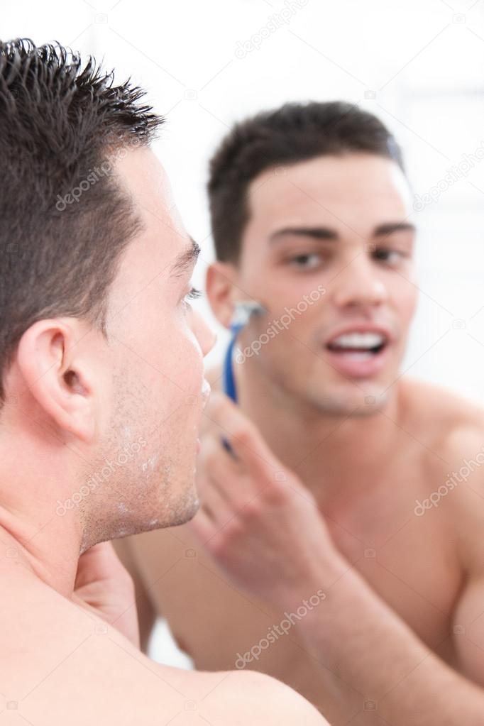 attractive man shaving in front of bathroom mirror