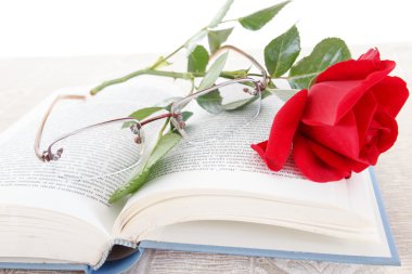 Açık kitap sayfalarında gözlük ile kitap ve kırmızı gül