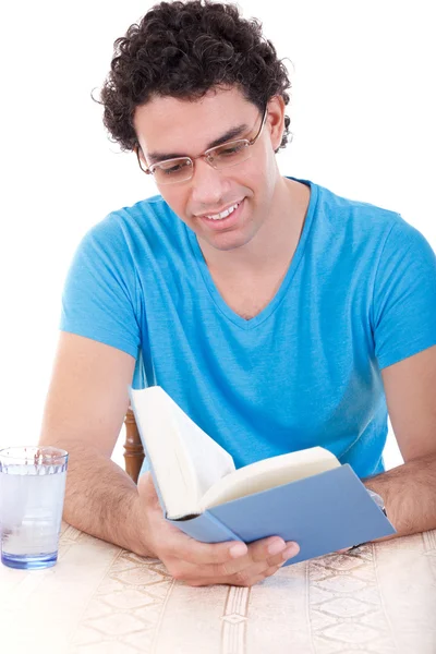 Hombre en camiseta azul sentado a la mesa y leyendo libro — Foto de Stock