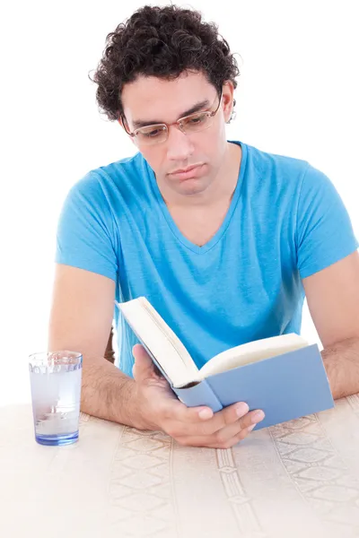 Homem sério em azul t-shirt sentado à mesa e livro de leitura — Fotografia de Stock