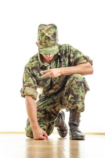 Soldado em uniforme de camuflagem e chapéu ajoelhado no chão e — Fotografia de Stock