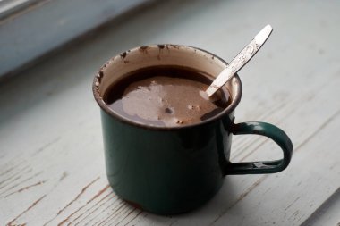 Pencere kenarında kahve olan eski bir diş minesi kupası.