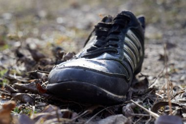 Eski siyah bir spor ayakkabı yolda yatıyor.