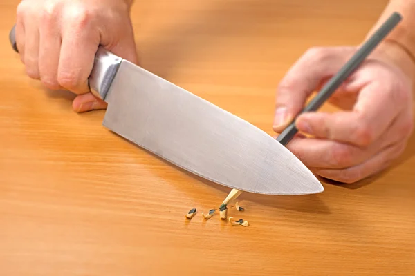 Затачивание карандаша ножом на столе — стоковое фото