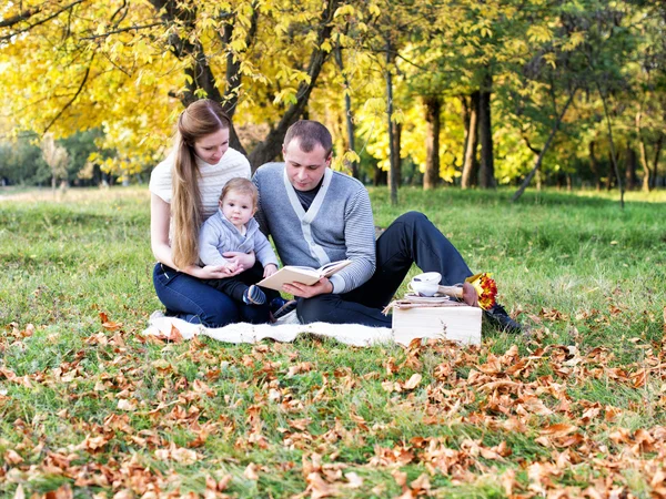 Lycklig familj i höst park läser en bok — Stockfoto