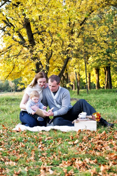 Happy family in autumn park reading a book — Stock Photo, Image