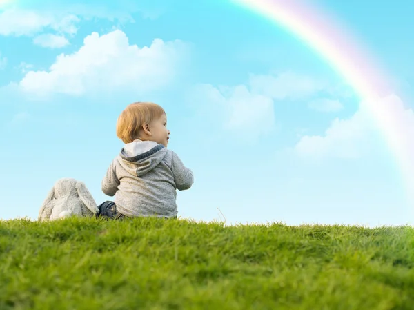Sevimli küçük çocuk oyuncak tavşan ile yeşil çimenlerin üzerine oturmuş — Stok fotoğraf
