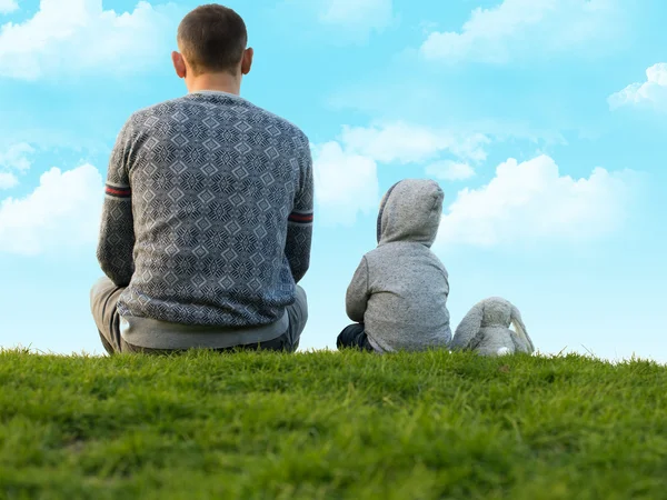 Niño pequeño con su padre sentado en la hierba verde — Foto de Stock