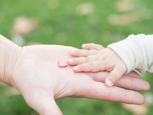 Adult hand holding a child's hand with a wooden heart — Stock Photo, Image