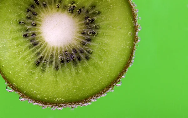 Primer plano de una rebanada de kiwi cubierta de burbujas de agua sobre un fondo verde — Foto de Stock