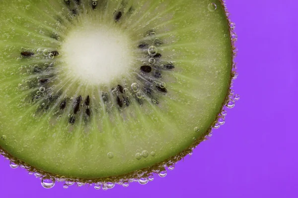 Närbild av en kiwi bit täckt av vatten bubblor mot en lila bakgrund — Stockfoto