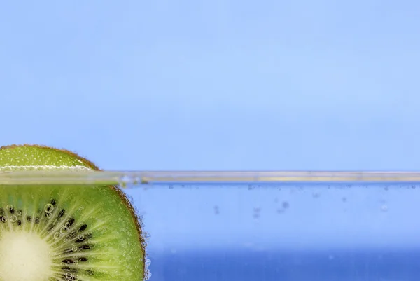 Nahaufnahme einer Kiwi-Scheibe, die in glitzerndem Wasser vor aquablauem Hintergrund schwimmt — Stockfoto