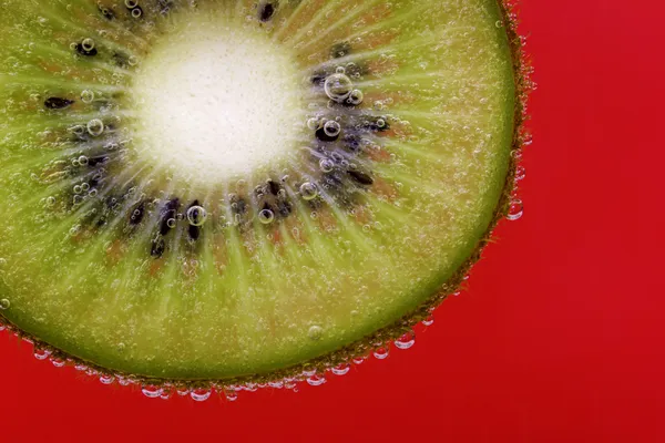 Närbild av en kiwi bit täckt av vatten bubblor mot en röd bakgrund — Stockfoto