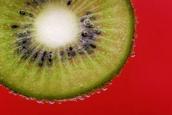 Primer plano de una rebanada de kiwi cubierta de burbujas de agua sobre un fondo rojo — Foto de Stock