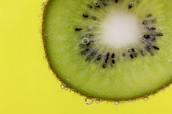 Nahaufnahme einer Kiwi-Scheibe mit Wasserblasen vor gelbem Hintergrund — Stockfoto
