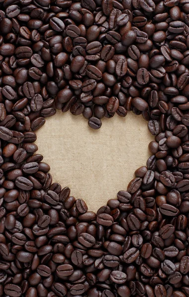 Pile of raw brown coffee beans in heart shape or love symbol on sack cloth — Stock Photo, Image