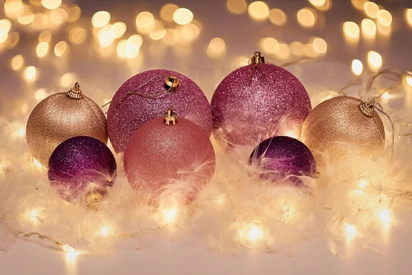 Pembe ve altın renginde Noel süsleri. Parlak sarı ışıkların etrafında, arka planda çelenkler....