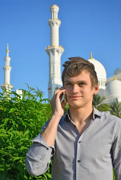 Joven sonriente con un teléfono celular frente a la mezquita — Foto de Stock