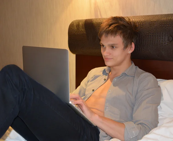 Jeune homme se relaxant au lit avec un ordinateur portable — Photo