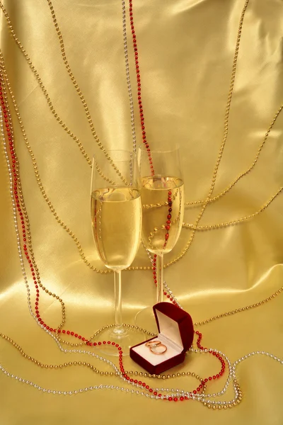 Wedding rings and stemware with sparkling wine on a golden background — Stock Photo, Image