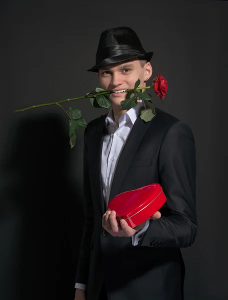 Молодой человек с розой в зубах держит коробку, как сердце любви — стоковое фото
