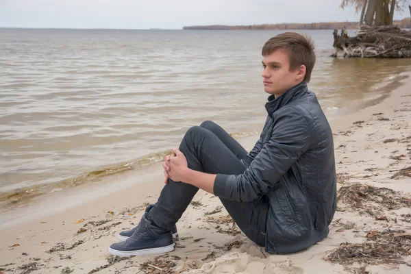 The guy who is sitting on the shore of the sea of autumn — Stock Photo, Image