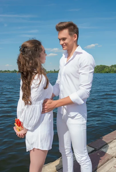 Guy hugs een meisje op een houten pier in de buurt van het water. — Stockfoto