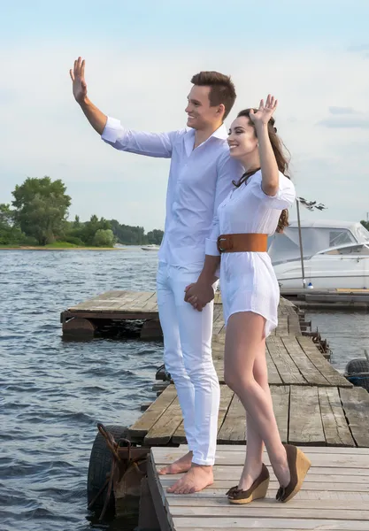 El tipo sostiene la mano de la chica en un muelle de madera cerca del agua . — Foto de Stock