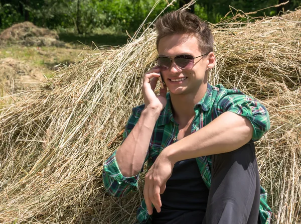 Young man talking on a cell phone while sitting in haystacks — Stock Photo, Image