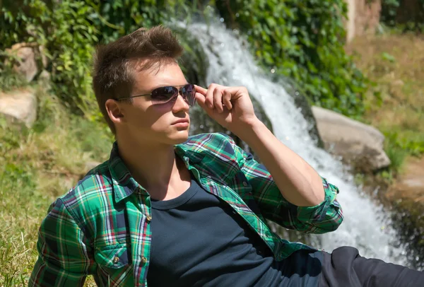 Guy in sunglasses relaxing in nature near the waterfall — Stock Photo, Image