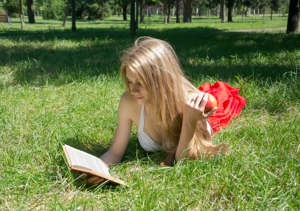 Menina segurando uma maçã vermelha e lendo um livro em um verão — Fotografia de Stock