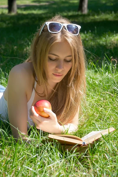 Dziewczyna trzyma czerwony jabłko i czytanie książki w parku lato — Zdjęcie stockowe