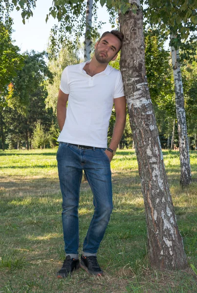 Young man standing at tree in park in summer — Stock Photo, Image