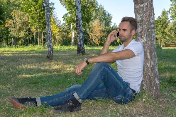 Young man sitting in the park with cell phone — Stock Photo, Image