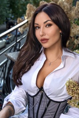 Güzel bir kadın, manken, korse içinde balkonda duruyor.