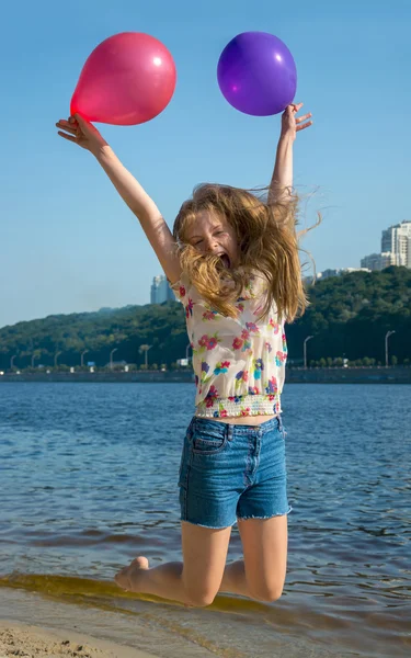 Glückliches Mädchen mit bunten Luftballons, die am Strand springen — Stockfoto