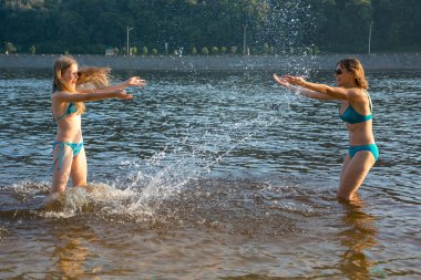 Annem ve kız birbirlerine plajda su ile sıçrama.