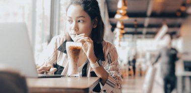 Buzlu kahve içen genç bir kadının portresi ve boş zamanlarının keyfini çıkarırken, düşünceli bir şekilde kahve dükkanının penceresinden dışarı bakan sosyal uzaklık konsepti..