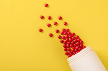 Kırmızı ilaç haplarının ve tabletlerin sarı arka plandaki ilaç şişesinden dökülmesi.