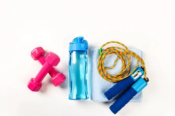 Fitness arka planının en üst görüntüsü. Spor salonu ve ev aletleri. Pembe dambıllar, su şişesi, atlama ipi, beyaz arka planda izole edilmiş havlu.
