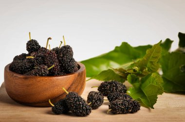 Taze organik dut meyvesi ve ahşap masa arkasında yeşil yapraklar.