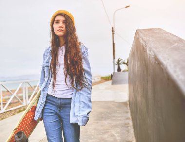 Kaykay parkında kaykay sürerken eğlenen kız, elinde kaykayıyla gülümseyen genç bayan kaykaycı portresi. Eğlence Faaliyeti Konsepti.