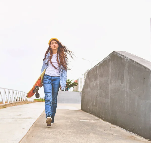 Ragazza che si diverte a cavalcare skateboard allo skate park, Ritratto di sorridere giovane skateboarder femminile tenendo il suo skateboard. Concetto di attività ricreativa. — Foto Stock