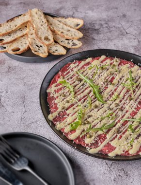 Carpaccio bifteği, parmesanlı soğuk aperatif, kapari ve roka, siyah tabakta seçici odaklanma.
