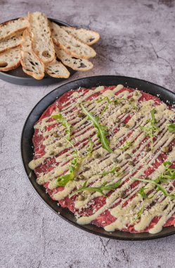 Carpaccio bifteği, parmesanlı soğuk aperatif, kapari ve roka, siyah tabakta seçici odaklanma.