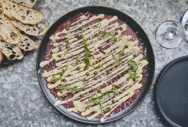 Carpaccio bifteği, parmesanlı soğuk aperatif, kapari ve roka, siyah tabakta seçici odaklanma.